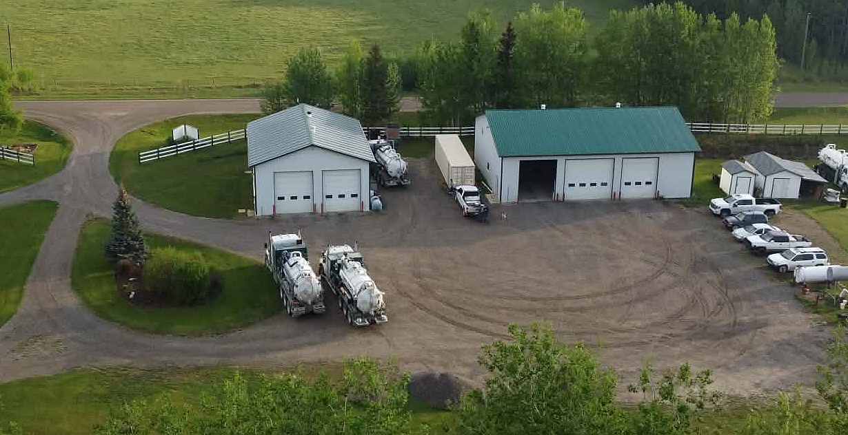 The Mateo Oilfield Services yard at Caroline, Alberta from the air: two shops, vacuum trucks and service vehicles on the gravel