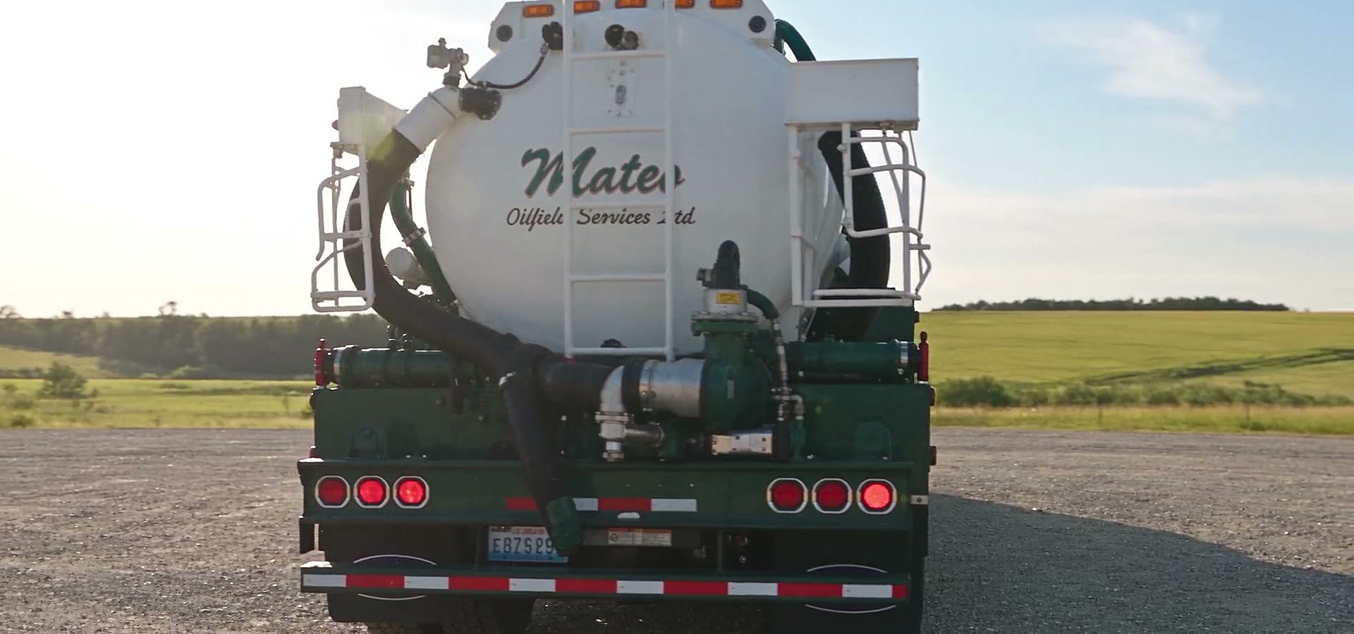 The rear of a Mateo vacuum unit on a gravel lease: the tank lettered Mateo Oilfield Services Ltd., the green pump deck, and reflective markings and lamps across the back